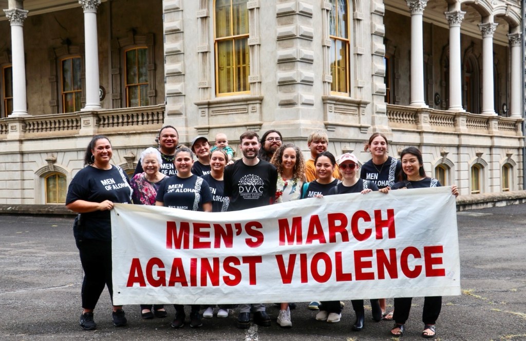 Group image of staff holding a men's march against violence banner fronting iolani palace.
